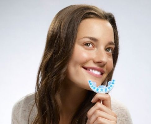 Smiling woman holding Glo teeth whitening application device